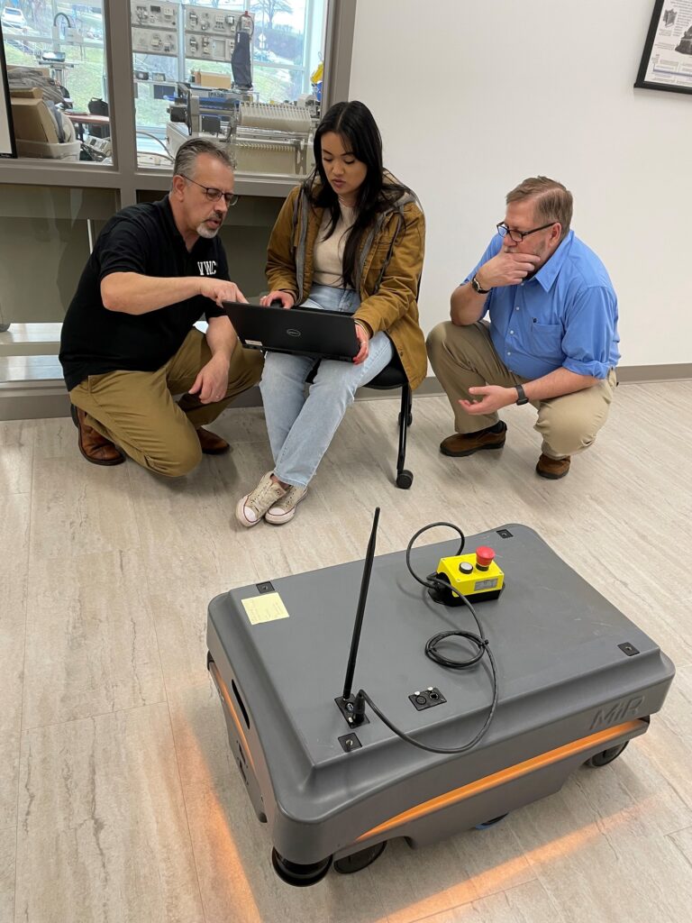 Dr. David Berry (left) helps Briana Wood and Adam O'Neal as the class fine-tunes a map of the STEM Building's hallway for the MiR 2000, a mobile industrial robot. A strip of light around the base emits colors that follow a code, such as a purple/yellow combination for an error.