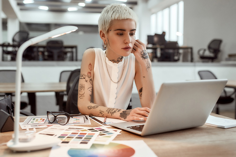 Student with short hair and tattoos looking at laptop